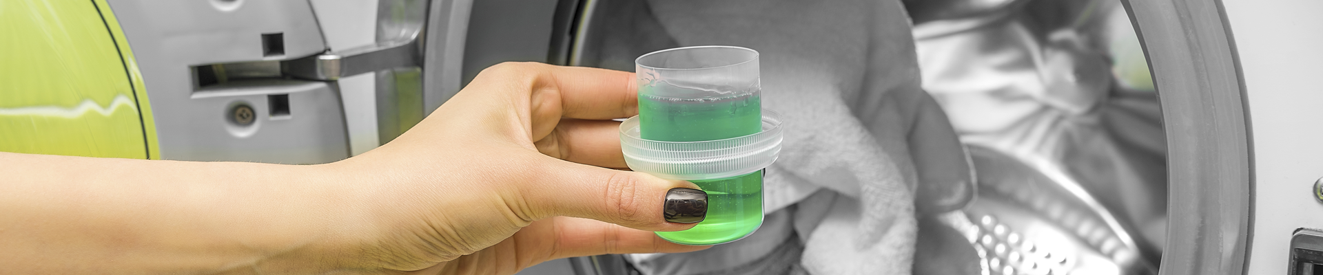 Person holding laundry detergent in front of a washing machine 
