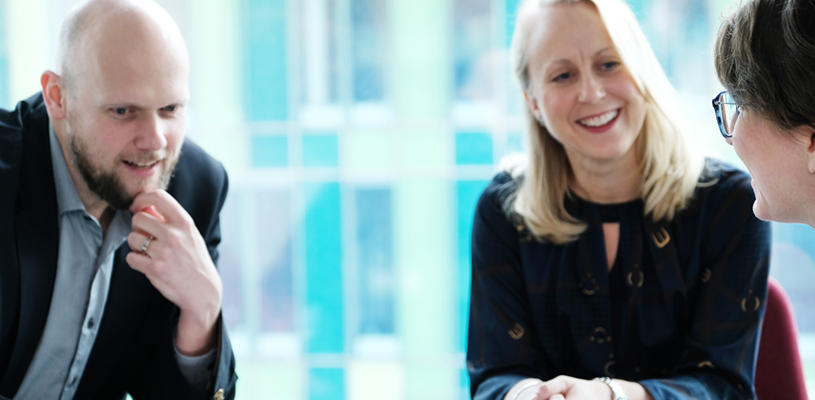 Photo of three colleagues sitting together and talking in an office 