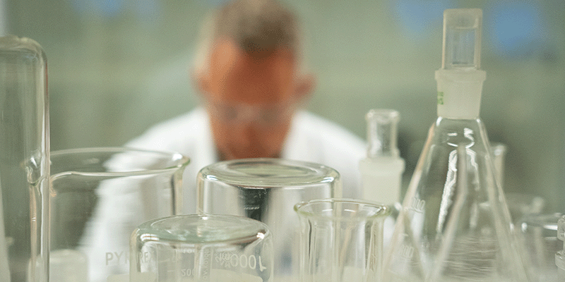 Various lab equipment in the foreground and a scientist in the background